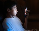 Jugendlicher im dunklen Zimmer blickt auf ein leuchtendes Smartphone