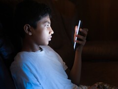 Jugendlicher im dunklen Zimmer blickt auf ein leuchtendes Smartphone