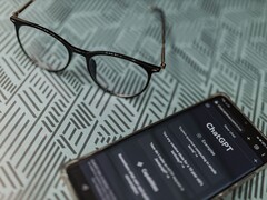 Smartphone mit geöffneter ChatGPT-App neben einer Brille auf einer gemusterten Fläche