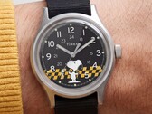 Nahaufnahme des schwarzen Zifferblatts der Timex MK1 mit Snoopy vor einer gelb-schwarz karierten Grafik sowie arabischen Stundenmarkierungen und Leuchtzeigern.