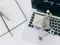 Miniatur-Einkaufswagen auf einer Laptop-Tastatur, auf dem Bildschirm steht Shop now