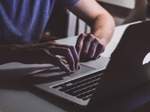 Hände tippen im Halbdunkel auf der Tastatur eines MacBooks, das Apple-Logo leuchtet