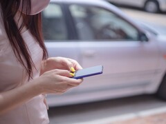 Eine Frau tippt auf ihrem Smartphone, im Hintergrund steht ein silbernes Auto