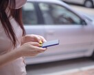 Eine Frau tippt auf ihrem Smartphone, im Hintergrund steht ein silbernes Auto
