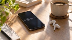 Smartphone mit Audio-Wellenform auf dem Display neben kabellosen Ohrhörern und einer Kaffeetasse auf einem Holzschreibtisch