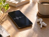 Smartphone mit Audio-Wellenform auf dem Display neben kabellosen Ohrhörern und einer Kaffeetasse auf einem Holzschreibtisch