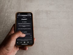 Hand hält ein Smartphone mit geöffneter ChatGPT-Oberfläche über einer grauen Steinfläche