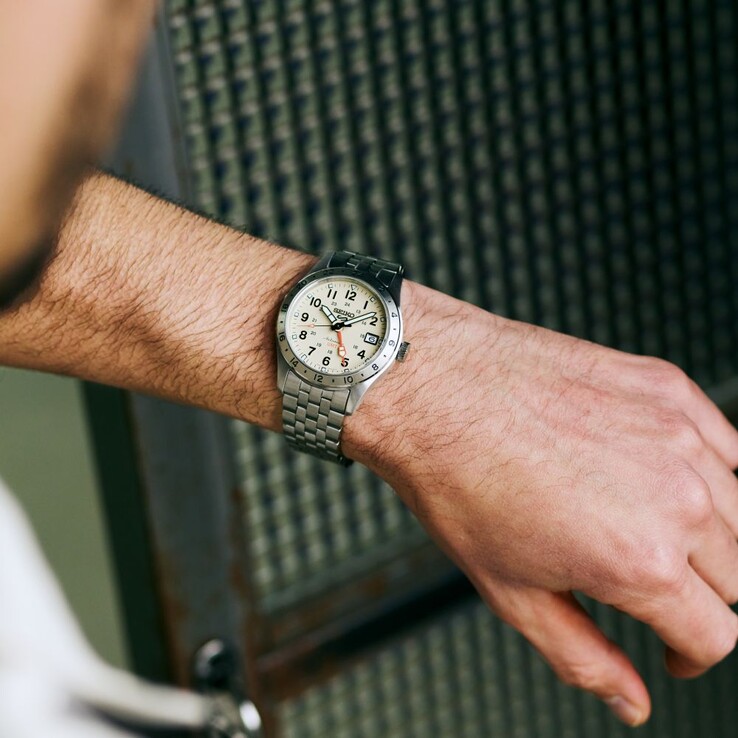 Vorderansicht der Seiko 5 Sports Field GMT HDB002 mit cremefarbenem Zifferblatt, orangefarbenem GMT-Zeiger, feststehender 24-Stunden-Lünette und Edelstahlarmband.