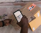 Hand hält ein Smartphone über ein Paket und scannt den Barcode