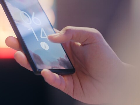 Hand hält ein Smartphone und entsperrt es per Fingerabdrucksensor auf dem Sperrbildschirm.