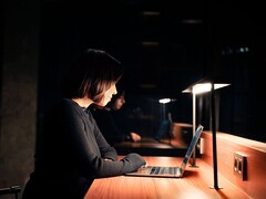 Frau arbeitet abends an einem Laptop im dunklen Büro
