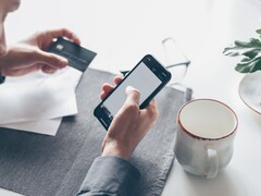 Person tippt auf einem Smartphone und hält in der anderen Hand eine Bankkarte