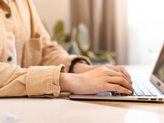 Hände tippen auf der Tastatur eines aufgeklappten Notebooks an einem hellen Schreibtisch