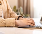Hände tippen auf der Tastatur eines aufgeklappten Notebooks an einem hellen Schreibtisch