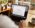 Person an einem Laptop mit geöffneter Google-Startseite, daneben eine Tasse Kaffee