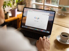 Person an einem Laptop mit geöffneter Google-Startseite, daneben eine Tasse Kaffee