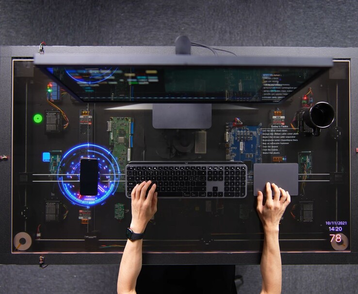 Der selbst gebaute, von AirPower inspirierte Schreibtisch von HTX Studio im Einsatz: Auf dem transparenten Display wird neben Tastatur, Trackpad und Monitor ein Smartphone geladen