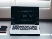 Aufgeklappter Laptop und Smartphone nebeneinander auf einem Schreibtisch bei Tageslicht