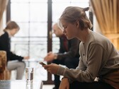Jugendliche schaut auf ihr Smartphone, im Hintergrund sitzen unscharf zwei Erwachsene