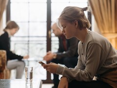 Jugendliche schaut auf ihr Smartphone, im Hintergrund sitzen unscharf zwei Erwachsene