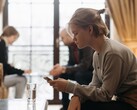 Jugendliche schaut auf ihr Smartphone, im Hintergrund sitzen unscharf zwei Erwachsene