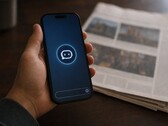 Hand hält ein Smartphone mit Chatbot-Symbol, daneben liegt eine gedruckte Zeitung.