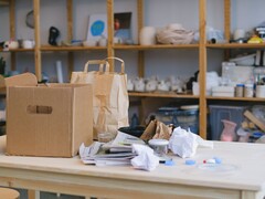 Pappkarton und Papiertüten auf einem Holztisch in einem Büro mit Regalen