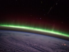 Ein von der ISS aufgenommenes Foto zeigt einen grünen Polarlichtbogen über den Wolken.