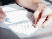Eine Hand unterschreibt ein Dokument mit einem blauen Kugelschreiber