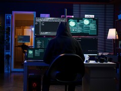 Eine vermummte Gestalt führt an einem Multi-Screen-Setup einen Cyberangriff durch