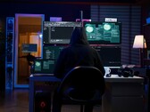 Eine vermummte Gestalt führt an einem Multi-Screen-Setup einen Cyberangriff durch
