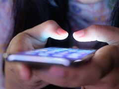 Zwei Hände halten ein Smartphone mit leuchtendem Bildschirm im Halbdunkel
