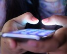 Zwei Hände halten ein Smartphone mit leuchtendem Bildschirm im Halbdunkel