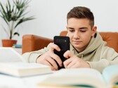 Jugendlicher im Hoodie tippt auf einem Smartphone, davor liegen aufgeschlagene Schulbücher