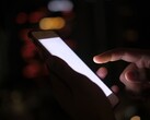 Hand hält ein Smartphone mit leuchtendem Bildschirm im Dunkeln