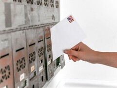 Hand steckt einen Briefumschlag in eine Reihe von Briefkästen