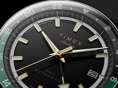 Nahaufnahme des schwarzen Zifferblatts der Timex Atelier GMT Première M1a mit goldfarbenen Zeigern, Leuchtindizes, einem Datumsfenster und einem schwarz-grünen 24-Stunden-GMT-Ring.