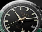 Nahaufnahme des schwarzen Zifferblatts der Timex Atelier GMT Première M1a mit goldfarbenen Zeigern, Leuchtindizes, einem Datumsfenster und einem schwarz-grünen 24-Stunden-GMT-Ring.
