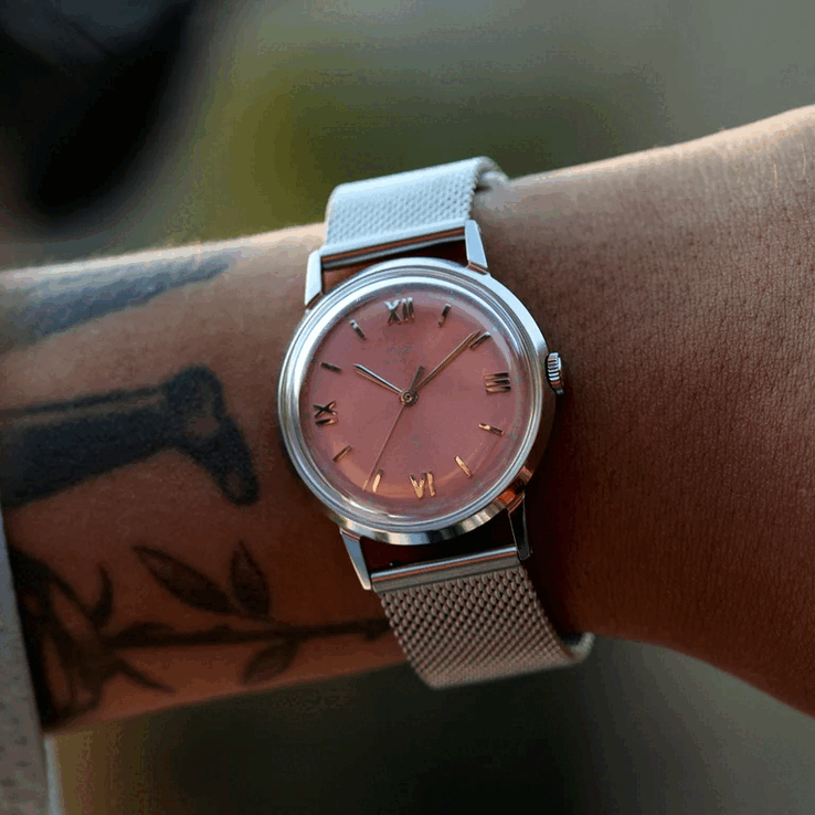 Eine Person, welche die Timex x Todd Snyder Marlin Mesh mit einem lachsfarbenen Sunburst-Zifferblatt und einem Mesh-Armband trägt.
