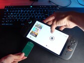Yu vom YouTube-Kanal Better Gaming hält eine Nintendo Switch 2 in der einen und einen grünen Open-Source-PCB-Adapter in der anderen Hand und versucht, ihn in den microSD Express-Steckplatz des Geräts zu stecken. (Bildquelle: Better Gaming via YouTube)