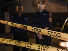 Zwei Polizisten stehen nachts hinter einem Absperrband mit der Aufschrift Stop