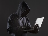 Ein vermummter Hacker arbeitet an einem Laptop vor dunklem, anonymem Hintergrund