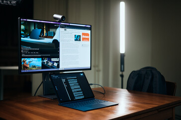 Lenovo Yoga Tab Plus Gen 2 auf einem Holztisch angeschlossen an einen großen externen Monitor, der Webseiten und Videos zeigt.