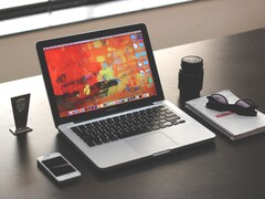 MacBook Pro auf einem dunklen Schreibtisch neben Smartphone, Brille und Notizbuch