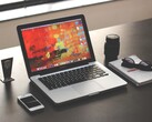 MacBook Pro auf einem dunklen Schreibtisch neben Smartphone, Brille und Notizbuch