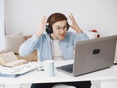 Mann mit Kopfhörern hebt frustriert die Hände vor einem Laptop