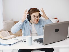 Mann mit Kopfhörern hebt frustriert die Hände vor einem Laptop