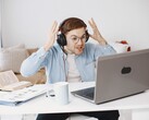 Mann mit Kopfhörern hebt frustriert die Hände vor einem Laptop