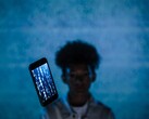 Schwebendes Smartphone mit Code auf dem Display vor blauem Hintergrund, dahinter eine unscharfe Person