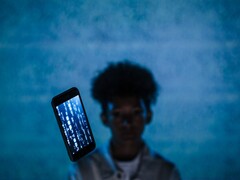 Schwebendes Smartphone mit Code auf dem Display vor blauem Hintergrund, dahinter eine unscharfe Person